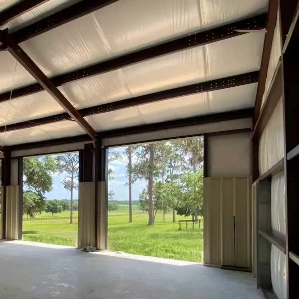 Empty metal barn interior with open doors looking out to a grassy field and trees