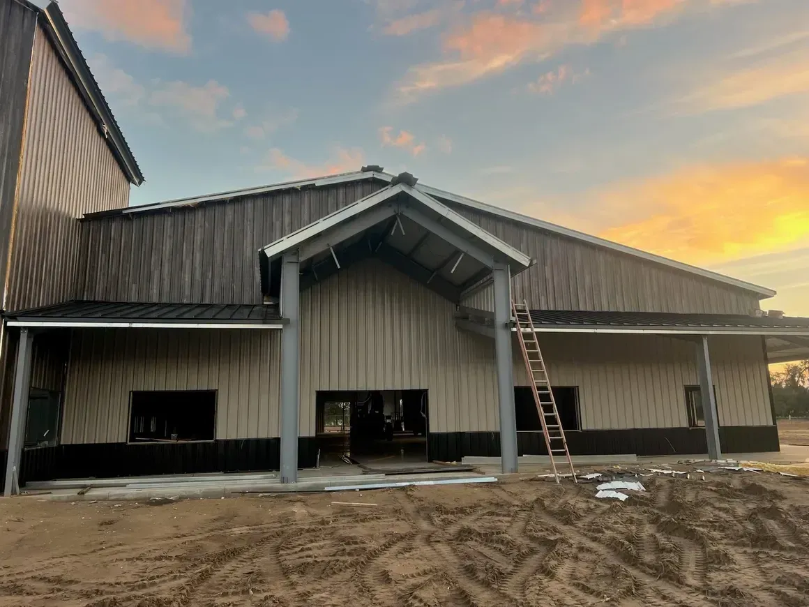Partially finished barn-style building with metal siding at sunset, ladder leaning against the front.