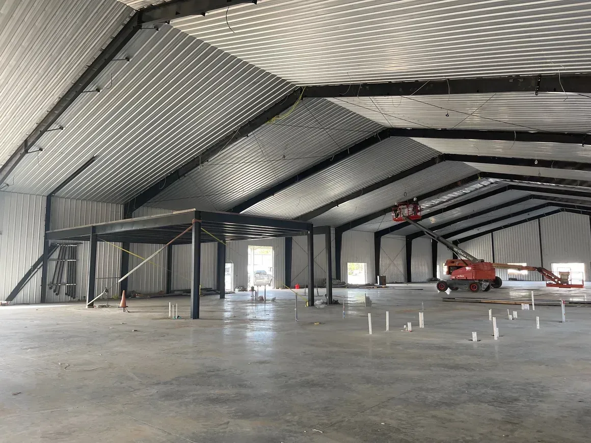 Empty metal warehouse interior with steel framing, concrete floor, and a red lift near the back.