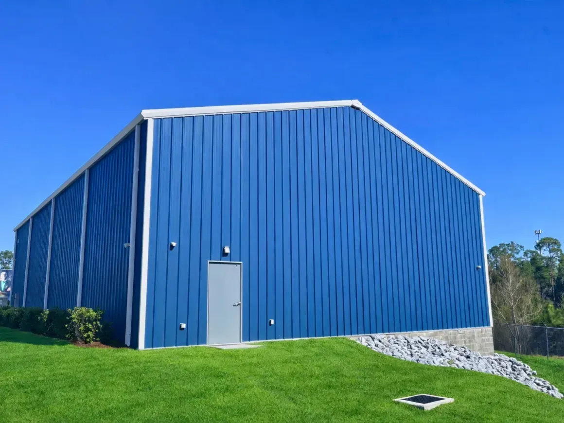 Blue metal warehouse with a gray door on a grassy hill under a clear blue sky