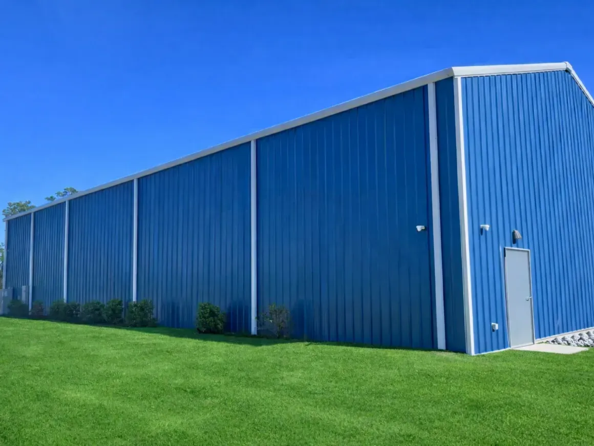 Blue metal warehouse beside a green lawn under a clear blue sky