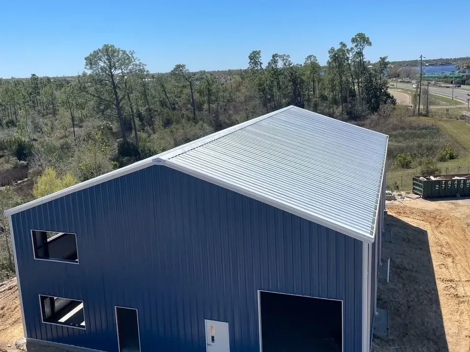 Blue metal warehouse with a white roof in a rural clearing, viewed from above