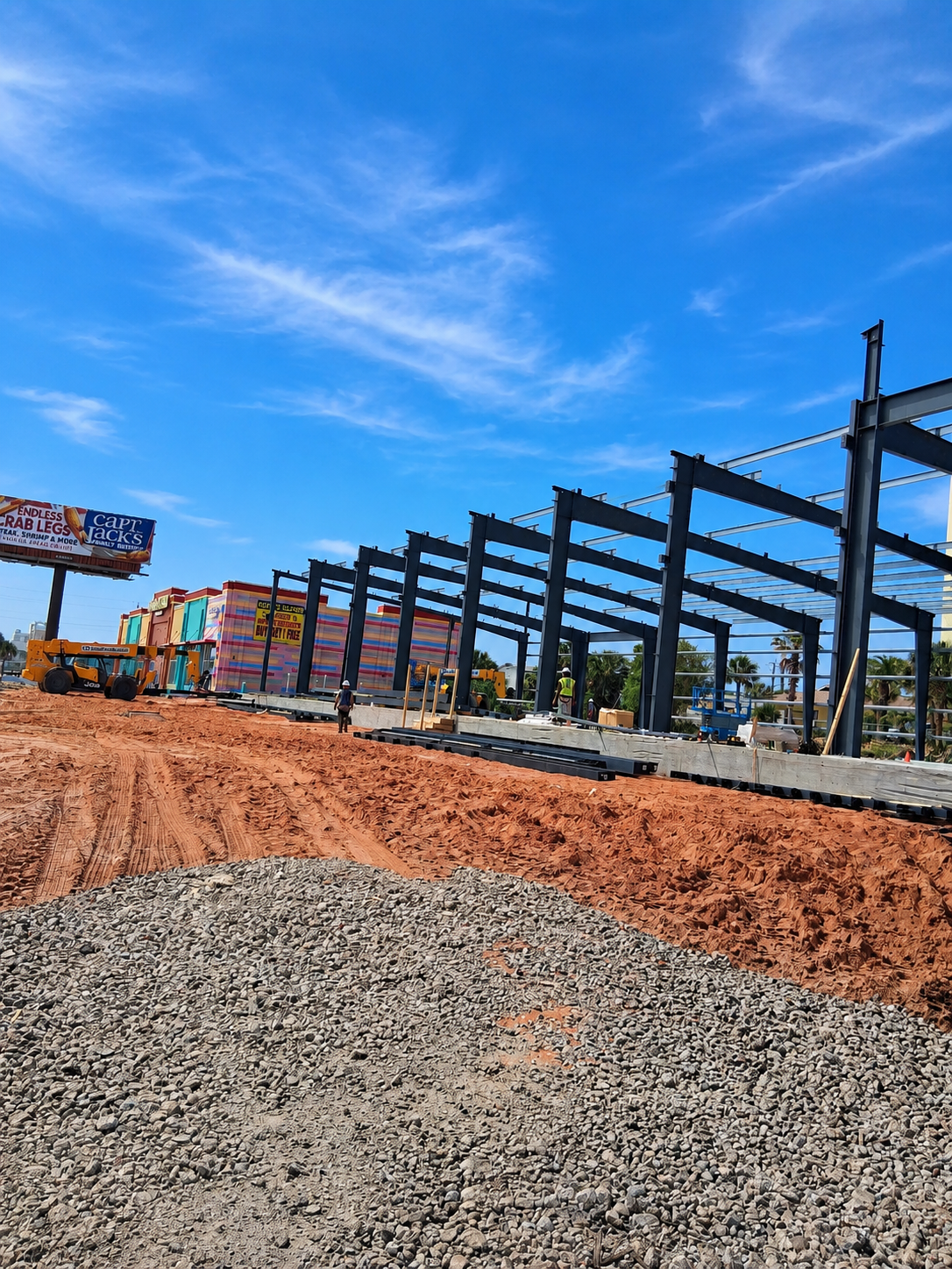 Construction site with steel framework, gravel foreground, and blue sky