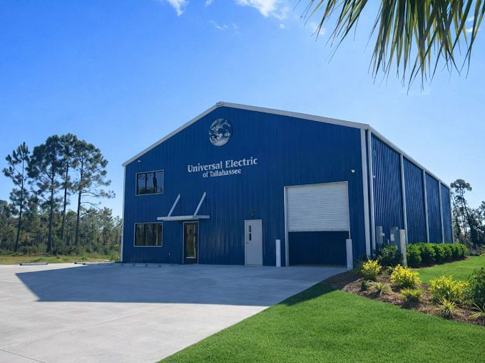 Blue industrial warehouse with a roll-up door, paved lot, and landscaped grass under a clear sky