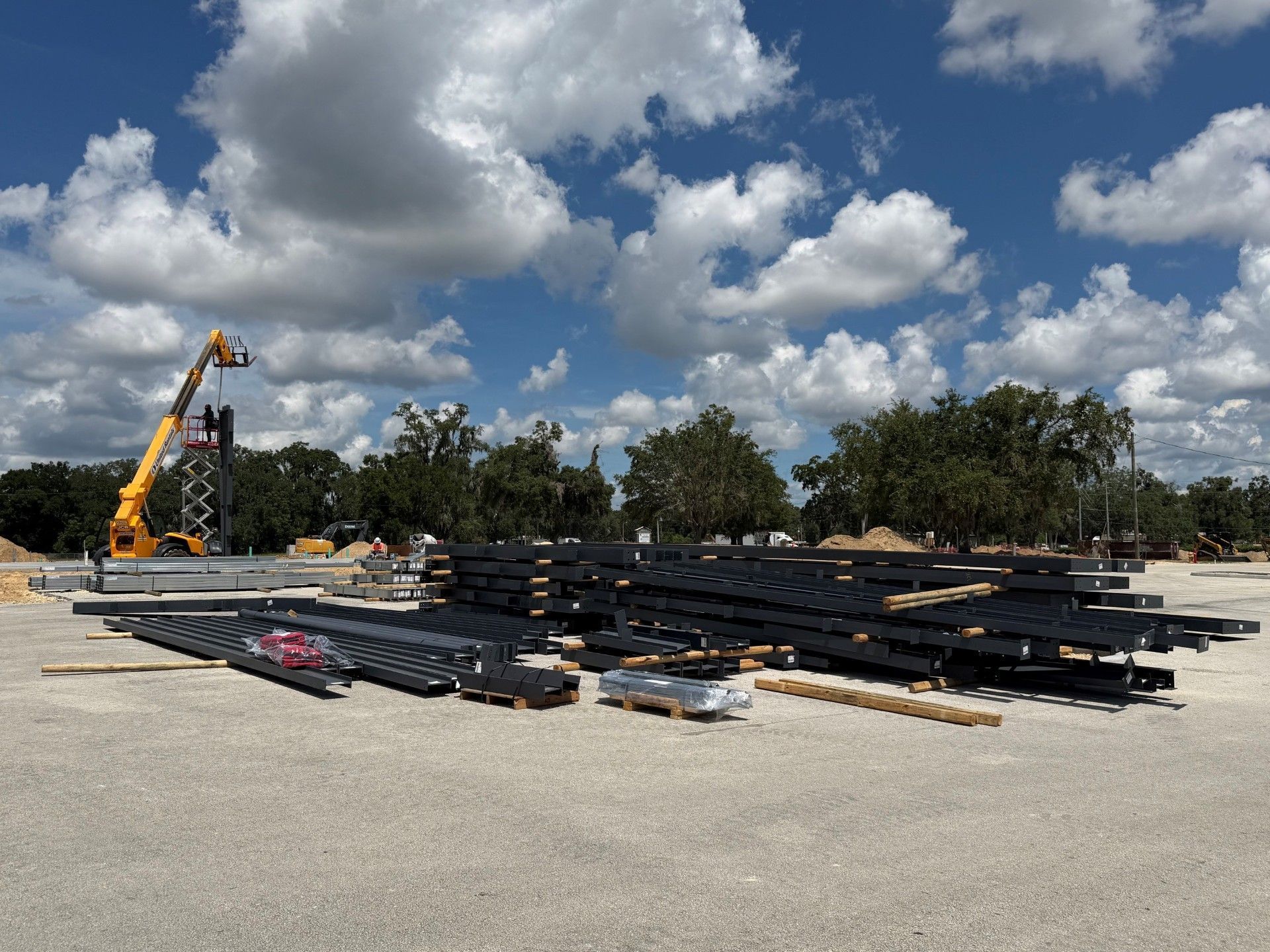 Construction site with stacked steel beams, a crane, and cloudy sky