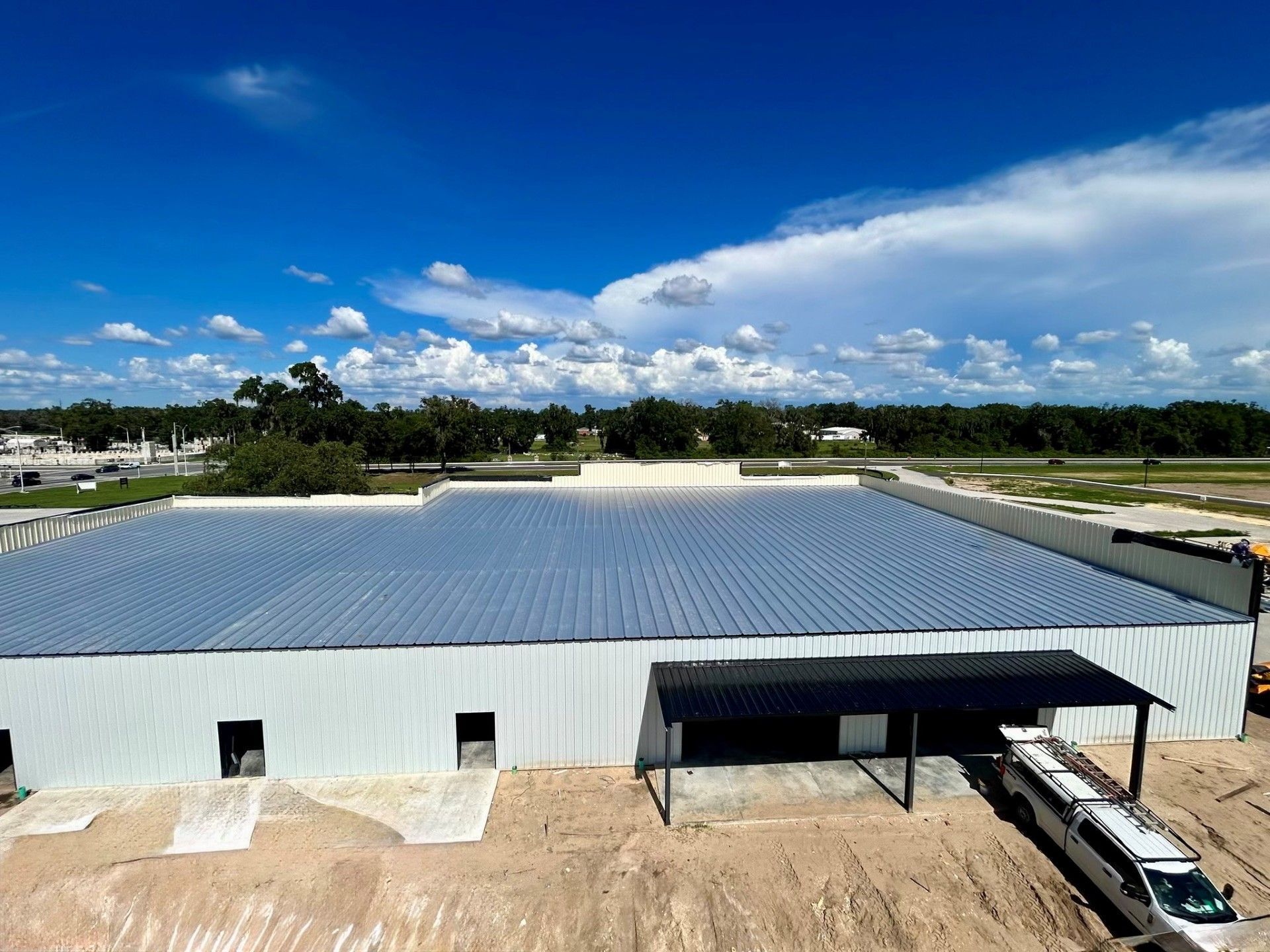 Aerial view of a large white industrial building with a blue roof under a partly cloudy sky
