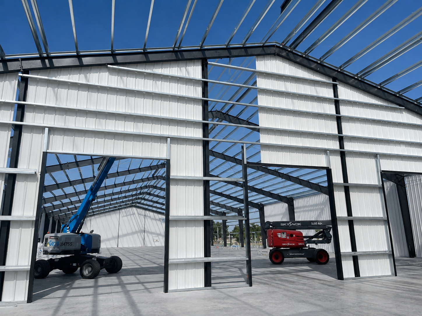 Inside a steel-frame warehouse, a blue and a red forklift sit in separate open bays.