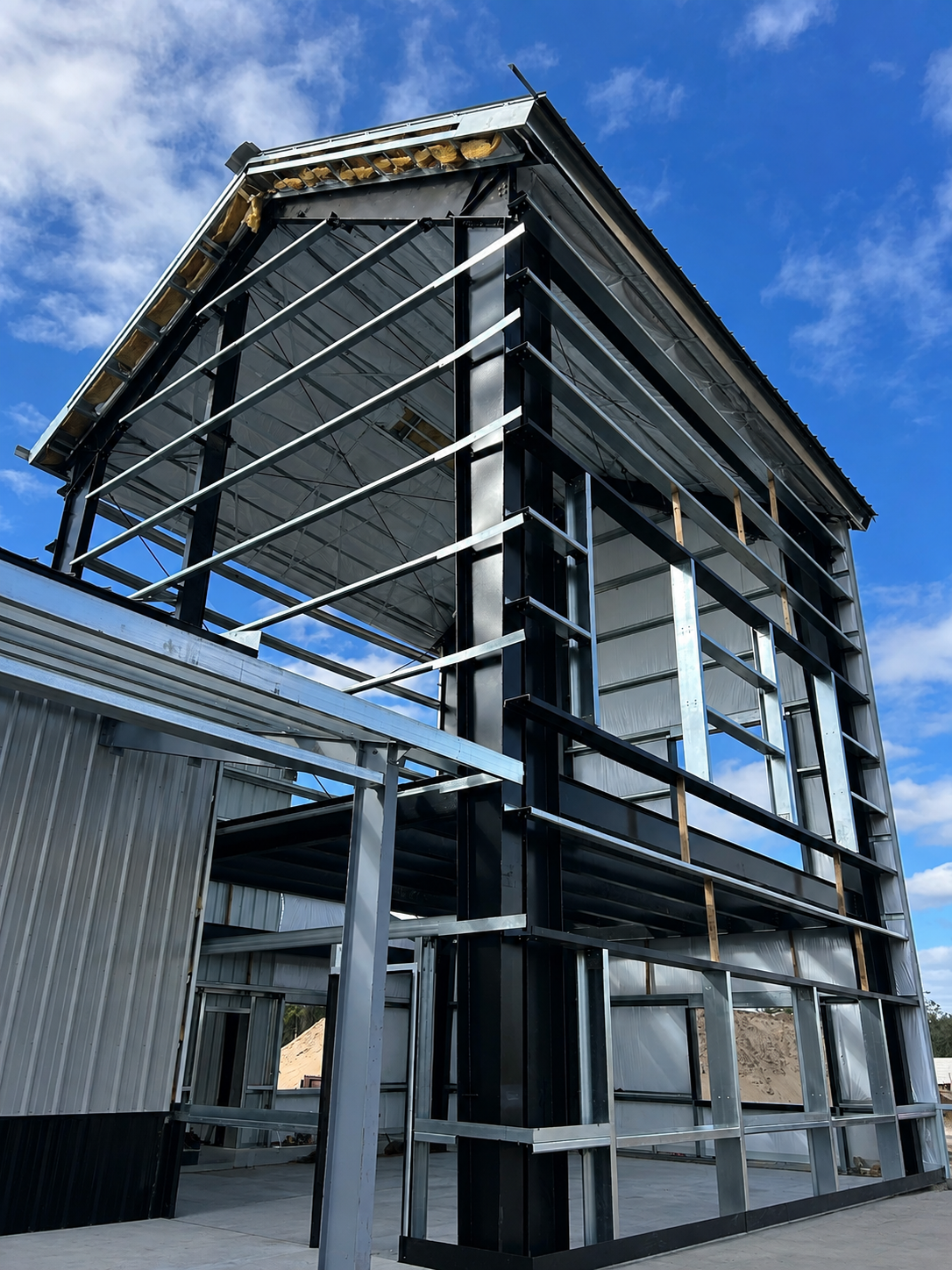 Modern metal building with exposed steel framing and sloped roof against a blue sky