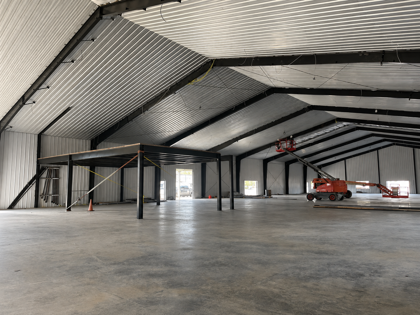Empty industrial warehouse with metal walls, concrete floor, and an orange lift parked inside.