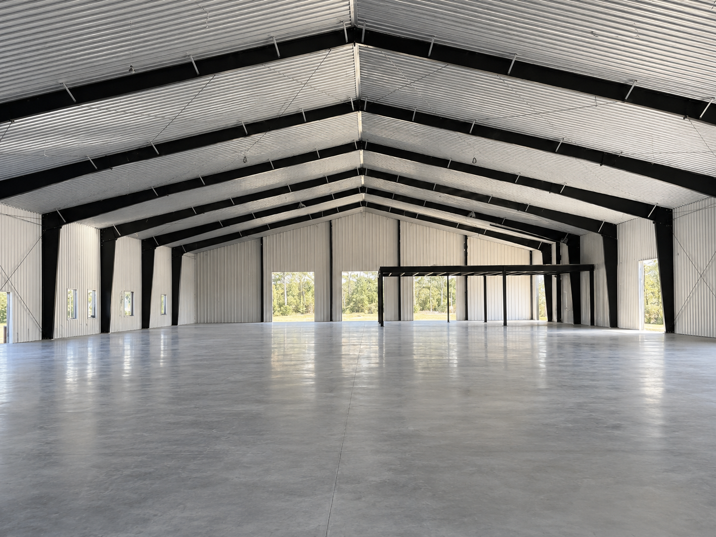 Empty industrial warehouse with high arched roof, concrete floor, and large open doorway at the far end