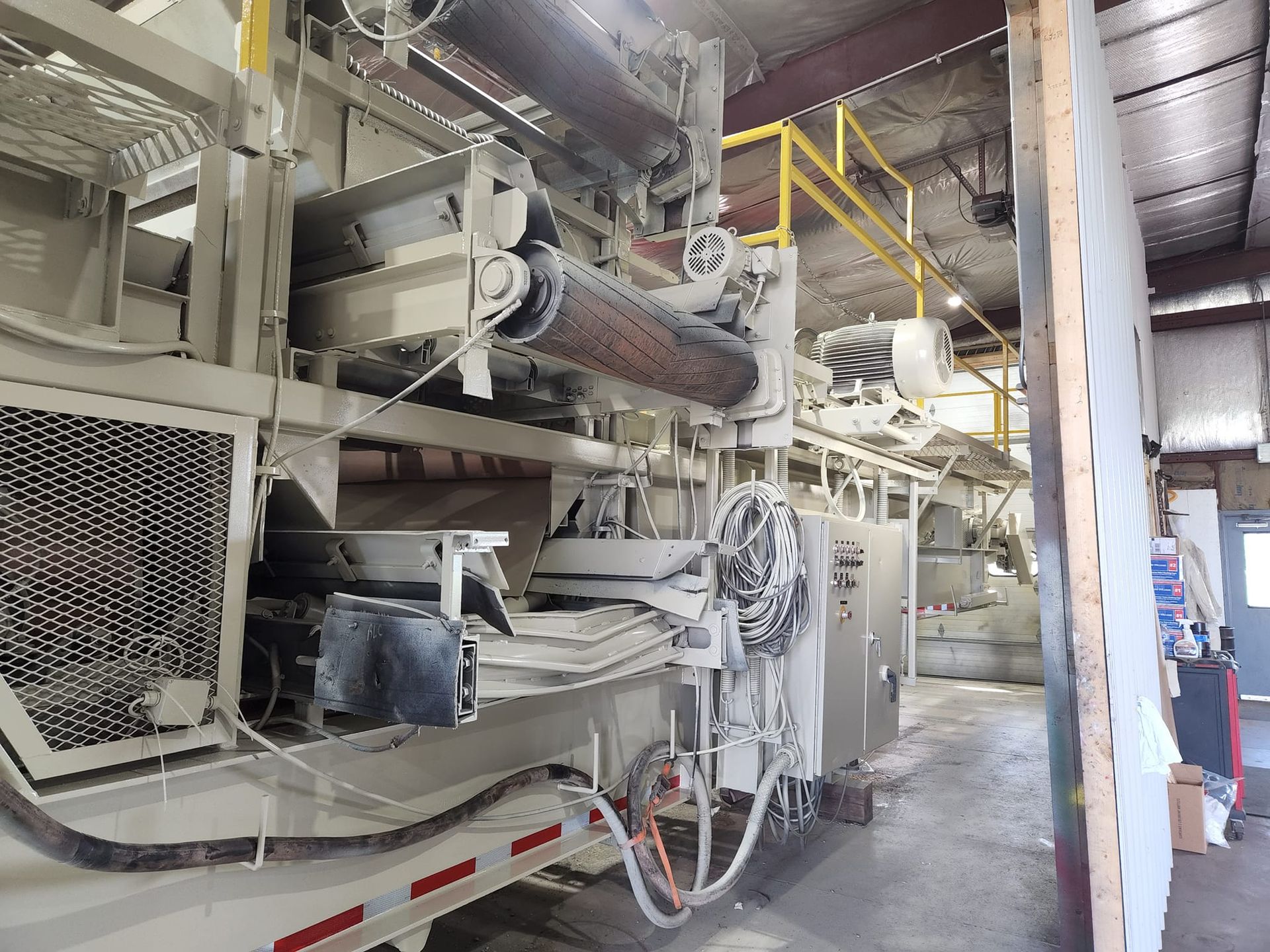 Industrial machinery with large rollers, conveyor belts, and wiring housed inside a warehouse-like facility.