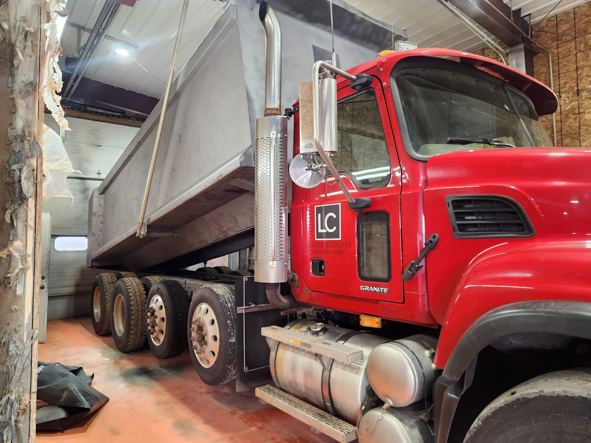 A bright red dump truck parked indoors, viewed from the side with its bed tilted upwards.