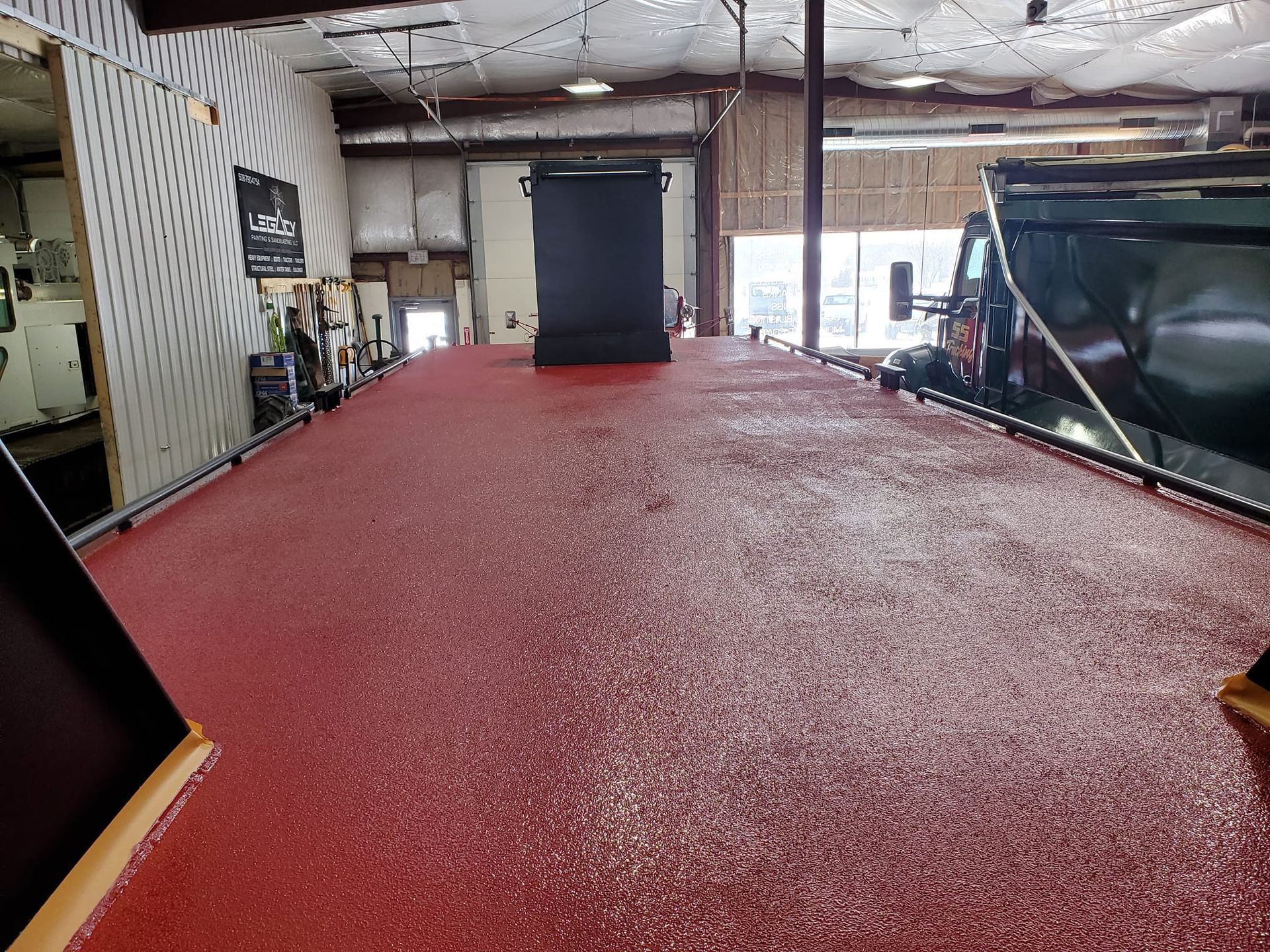 A large, textured red surface coating in a workshop, with a black divider panel in the background.