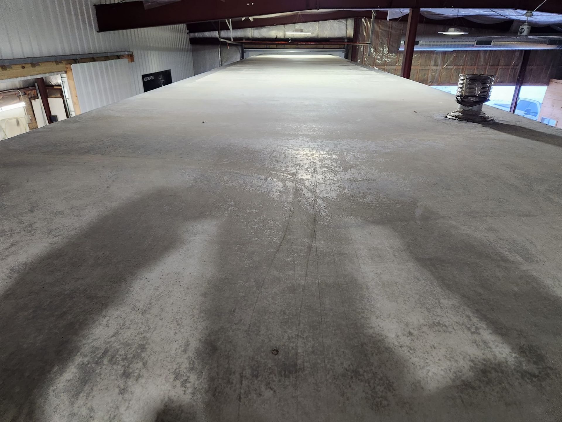 A high-angle view looking down the length of a long, flat concrete surface inside a structure with steel roof supports.