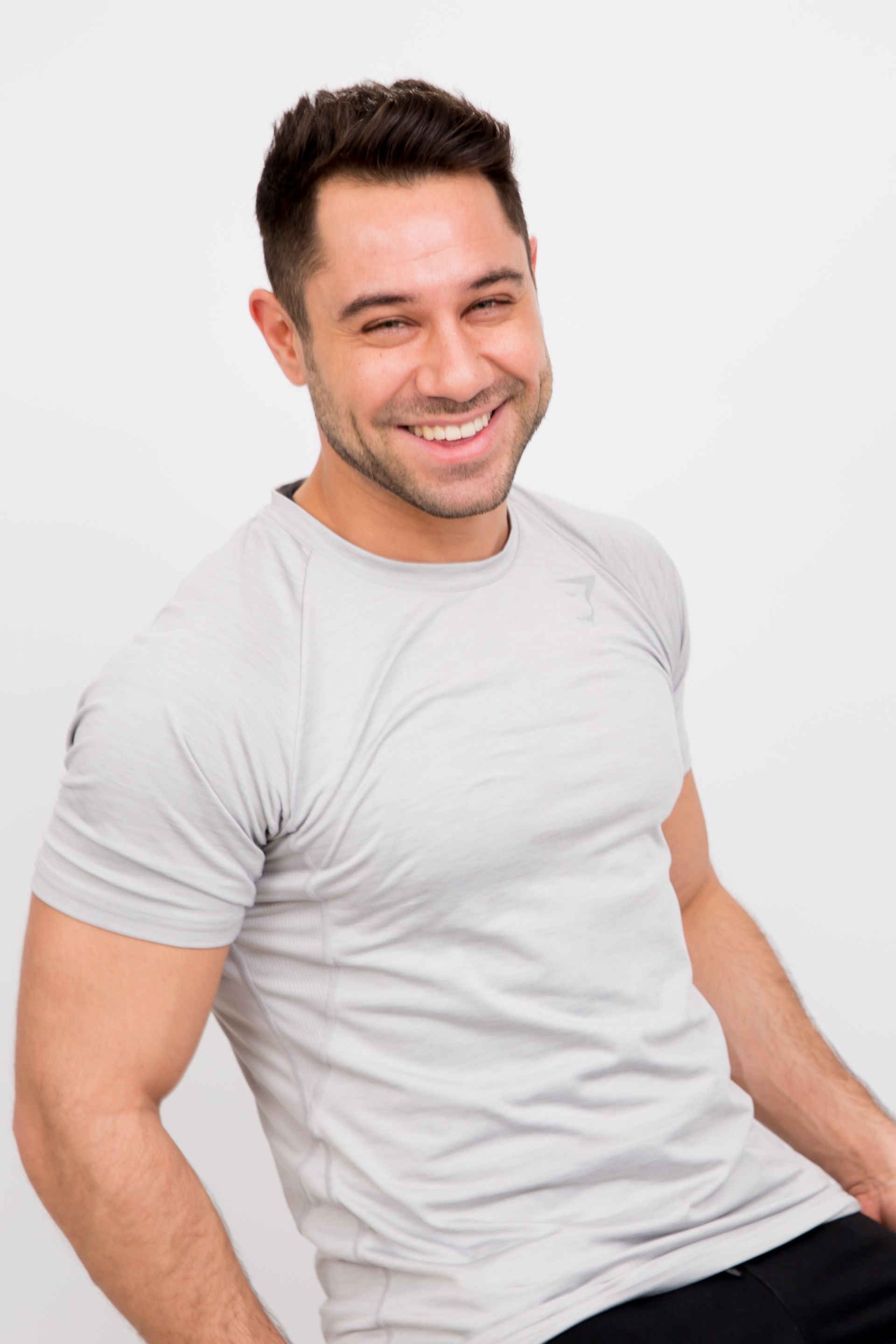 A man is wearing a grey t-shirt and smiling.