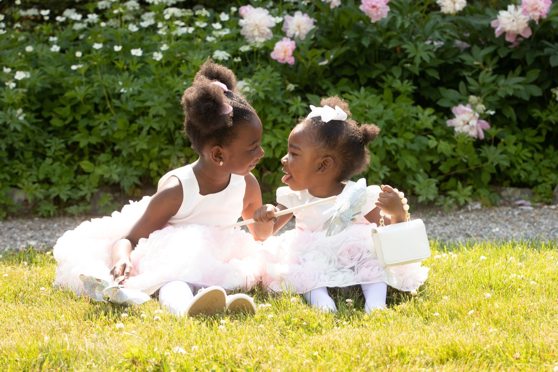 Two little girls are sitting in the grass talking to each other.