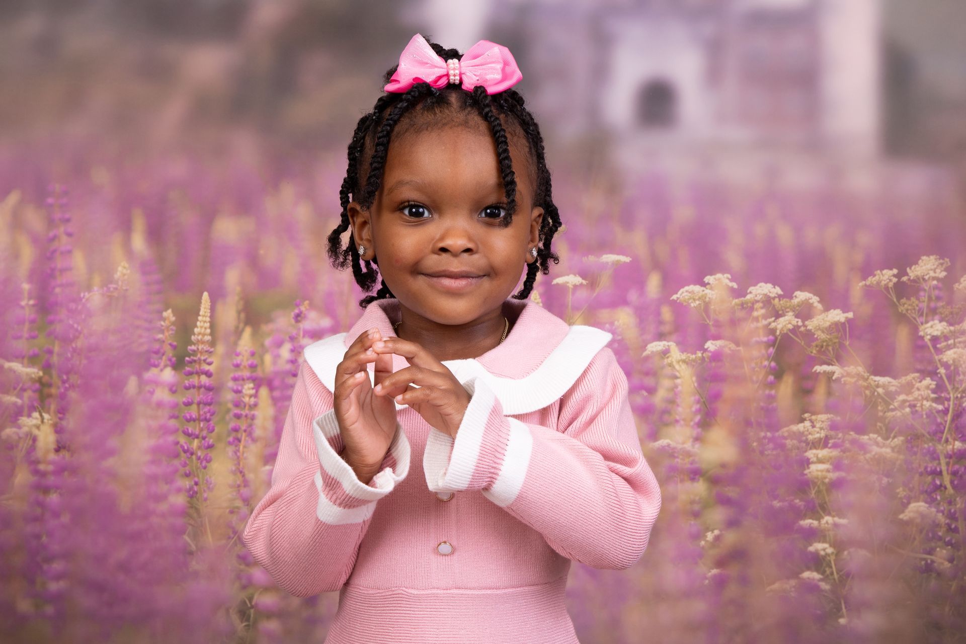 A little girl in a pink dress is standing in a field of purple flowers.