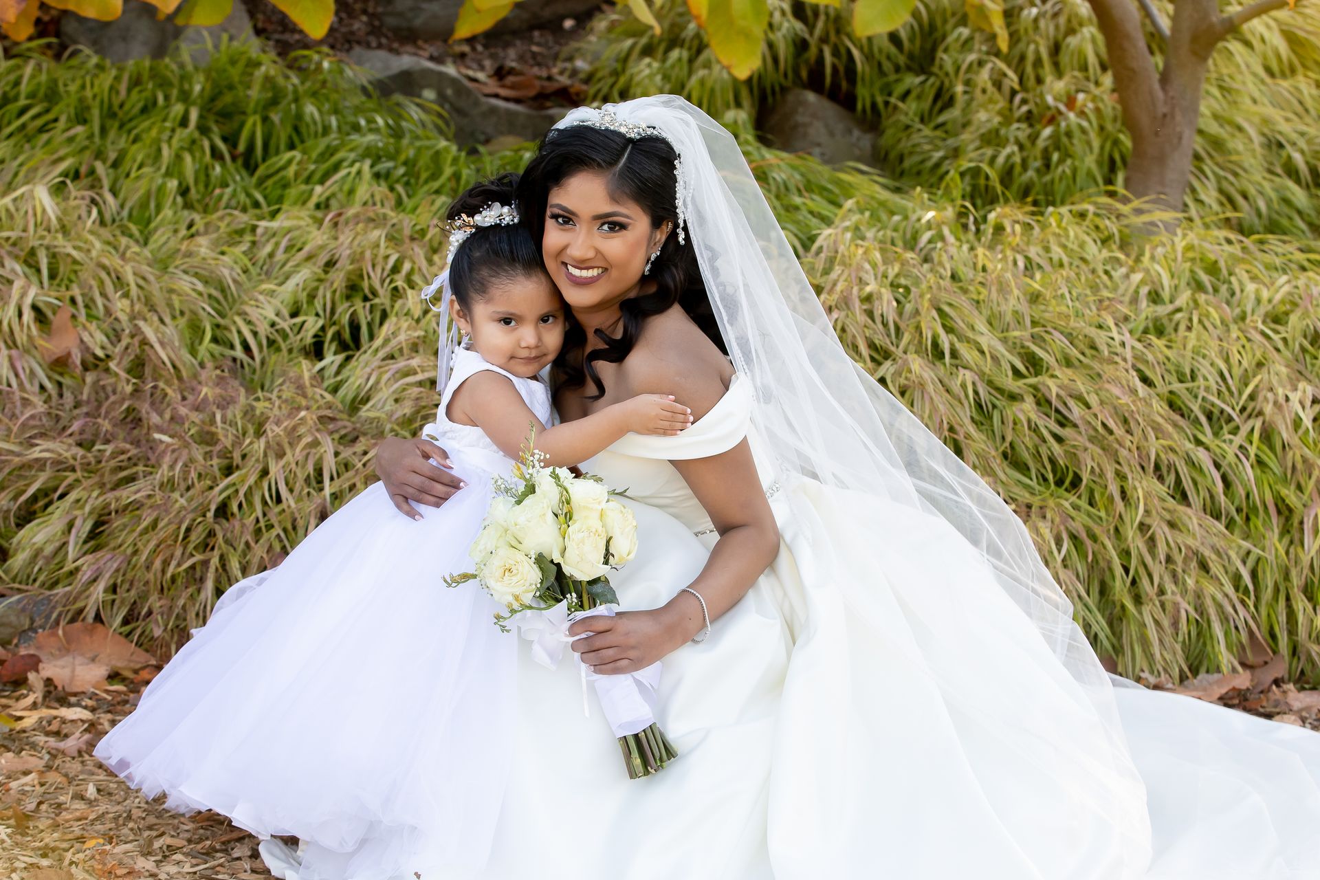 A bride and her flower girl are posing for a picture.