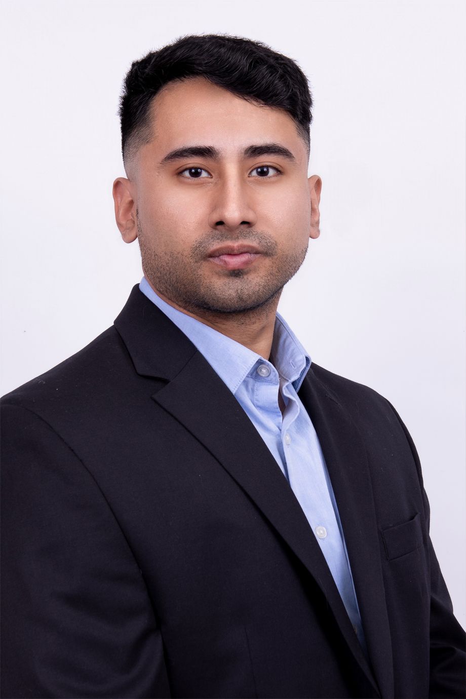A man in a suit and blue shirt is standing in front of a white background.