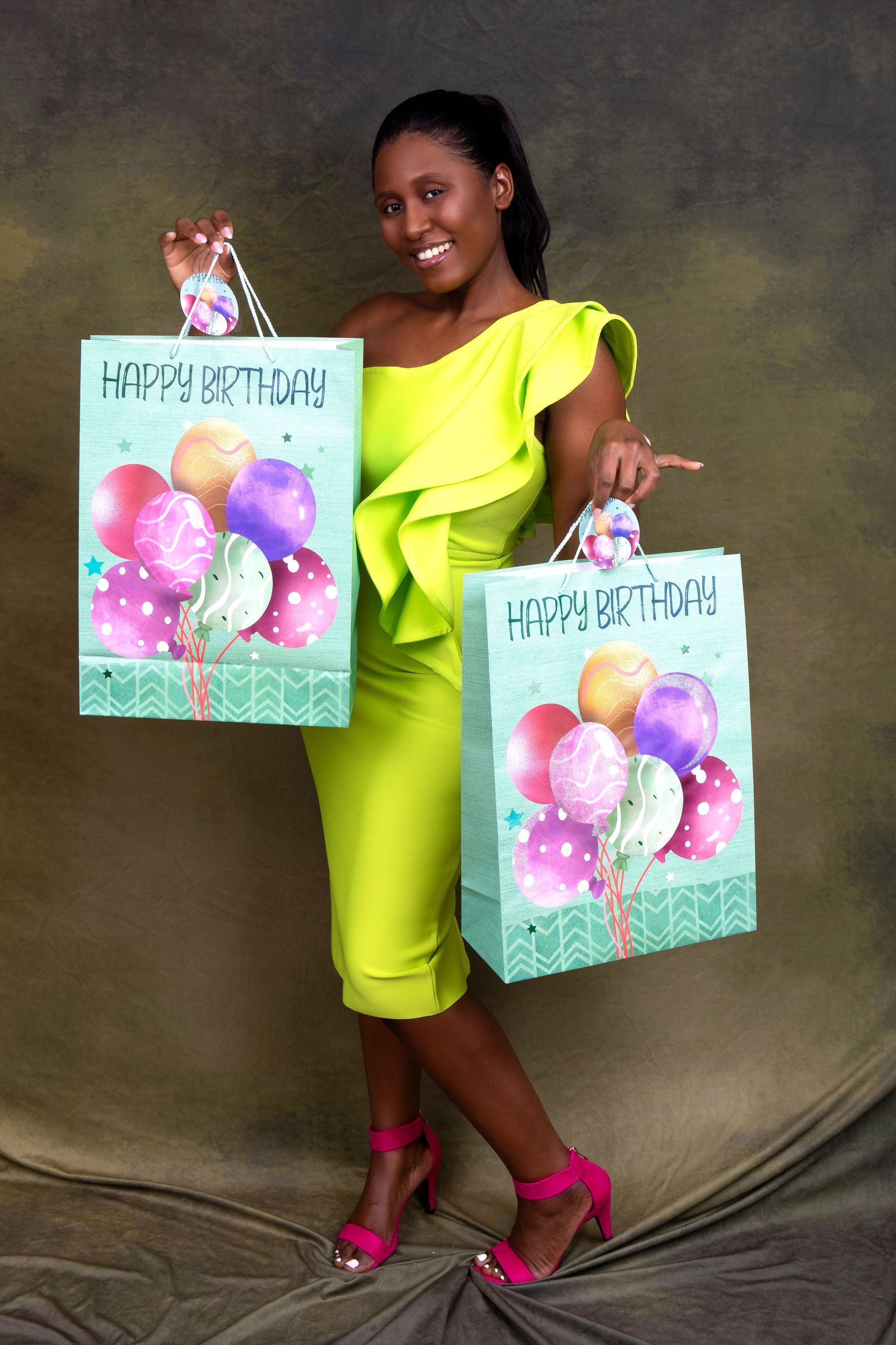 A woman in a green dress is holding two happy birthday bags