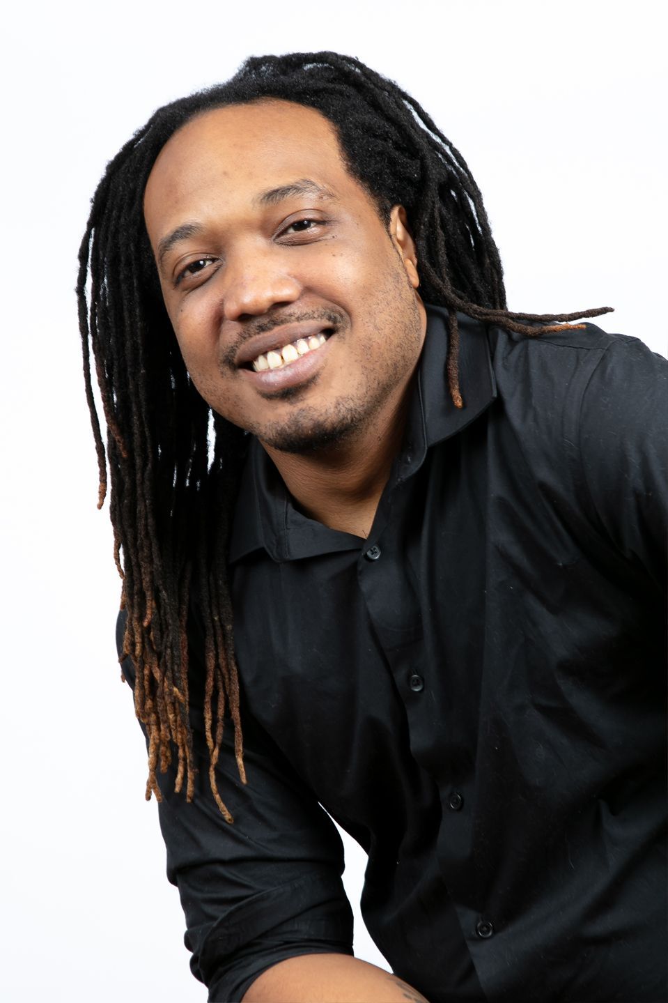 A man with dreadlocks is wearing a black shirt and smiling