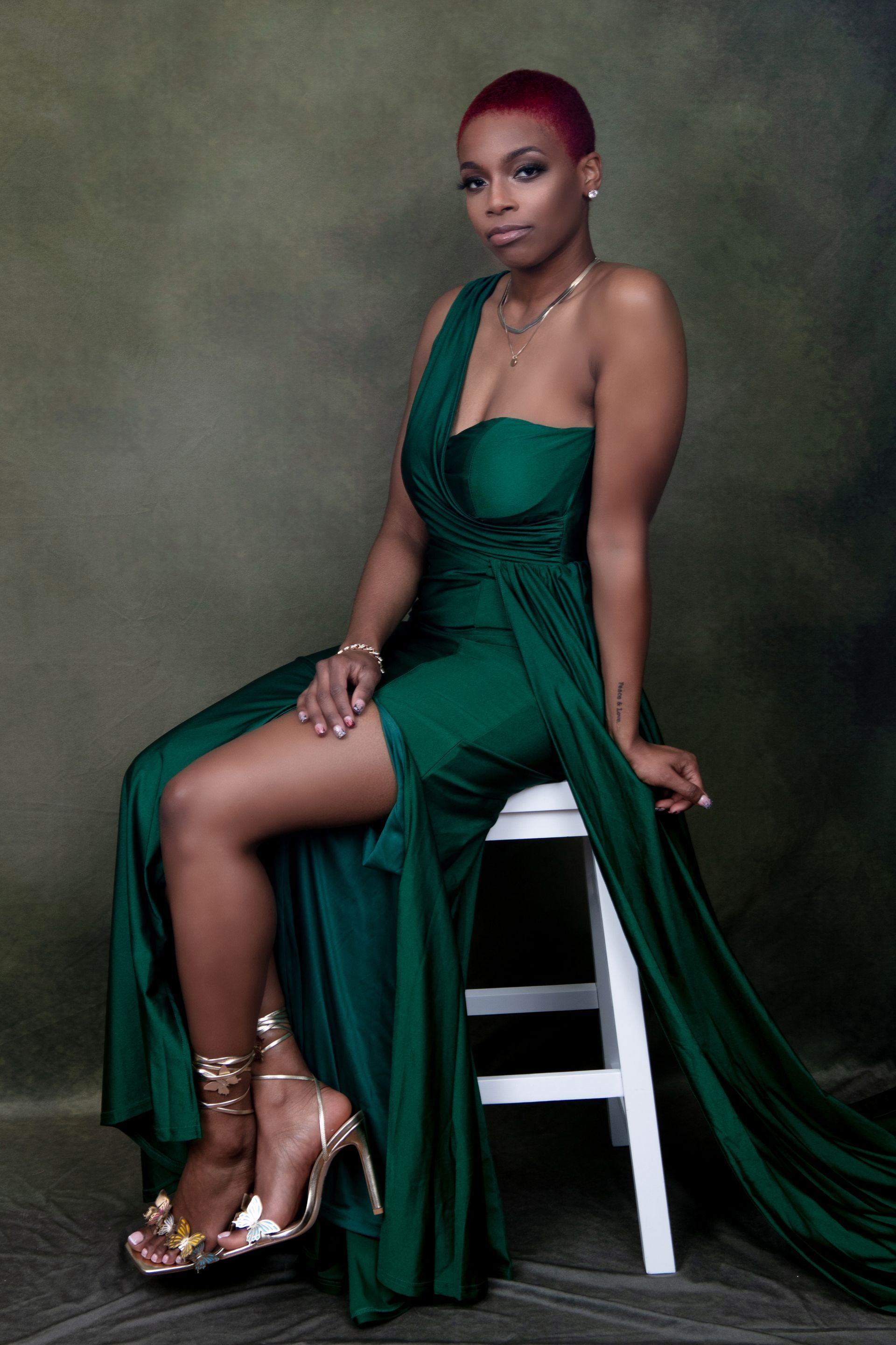 A woman in a green dress is sitting on a white stool.