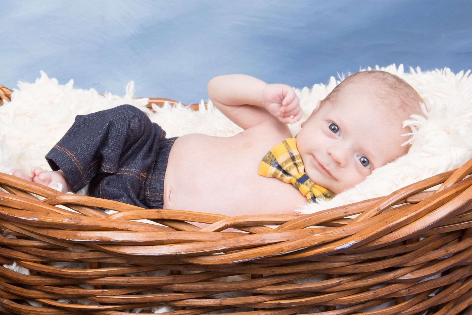 A baby wearing a bow tie is laying in a basket.