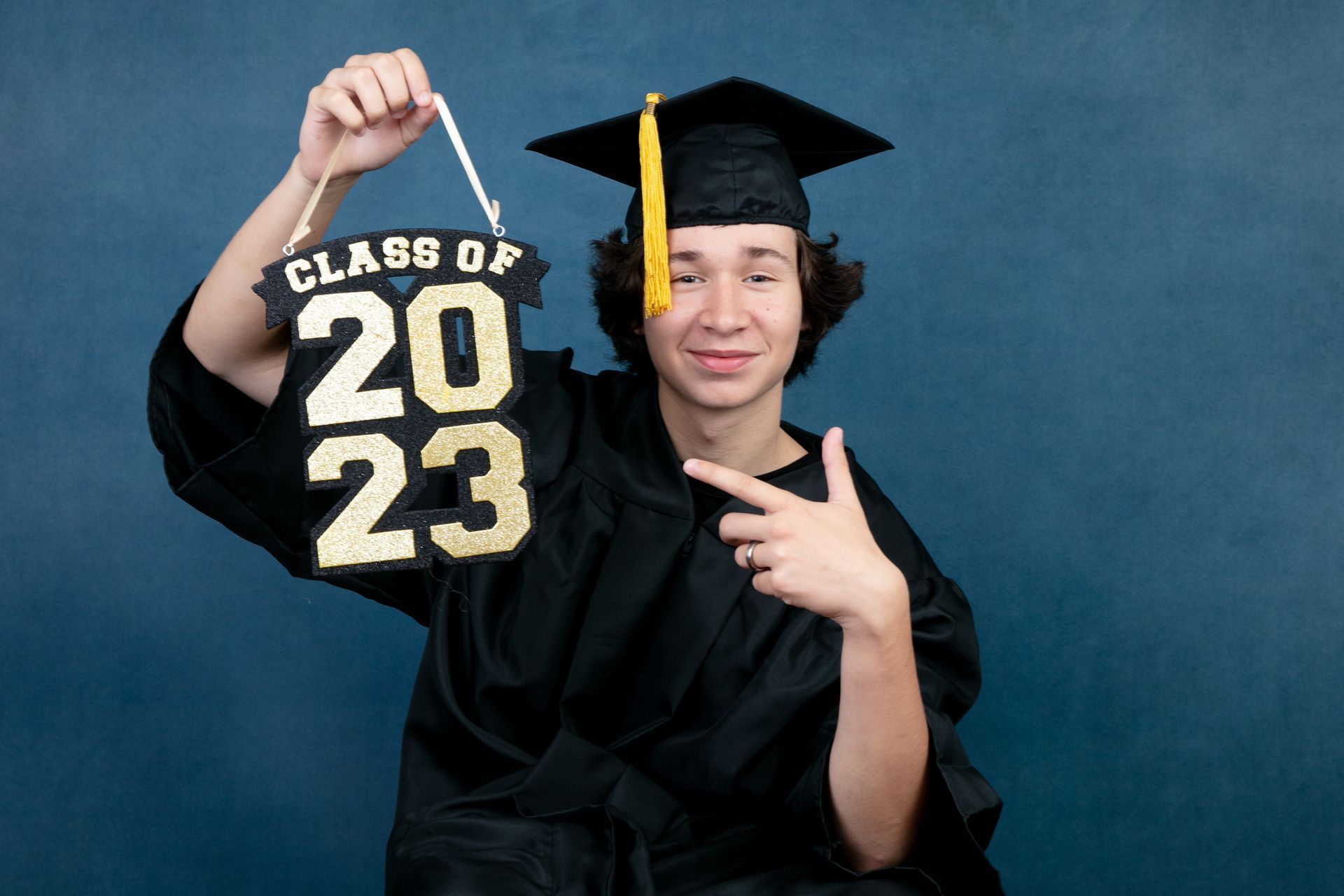 A young man in a graduation cap and gown is holding a sign that says class of 2023.
