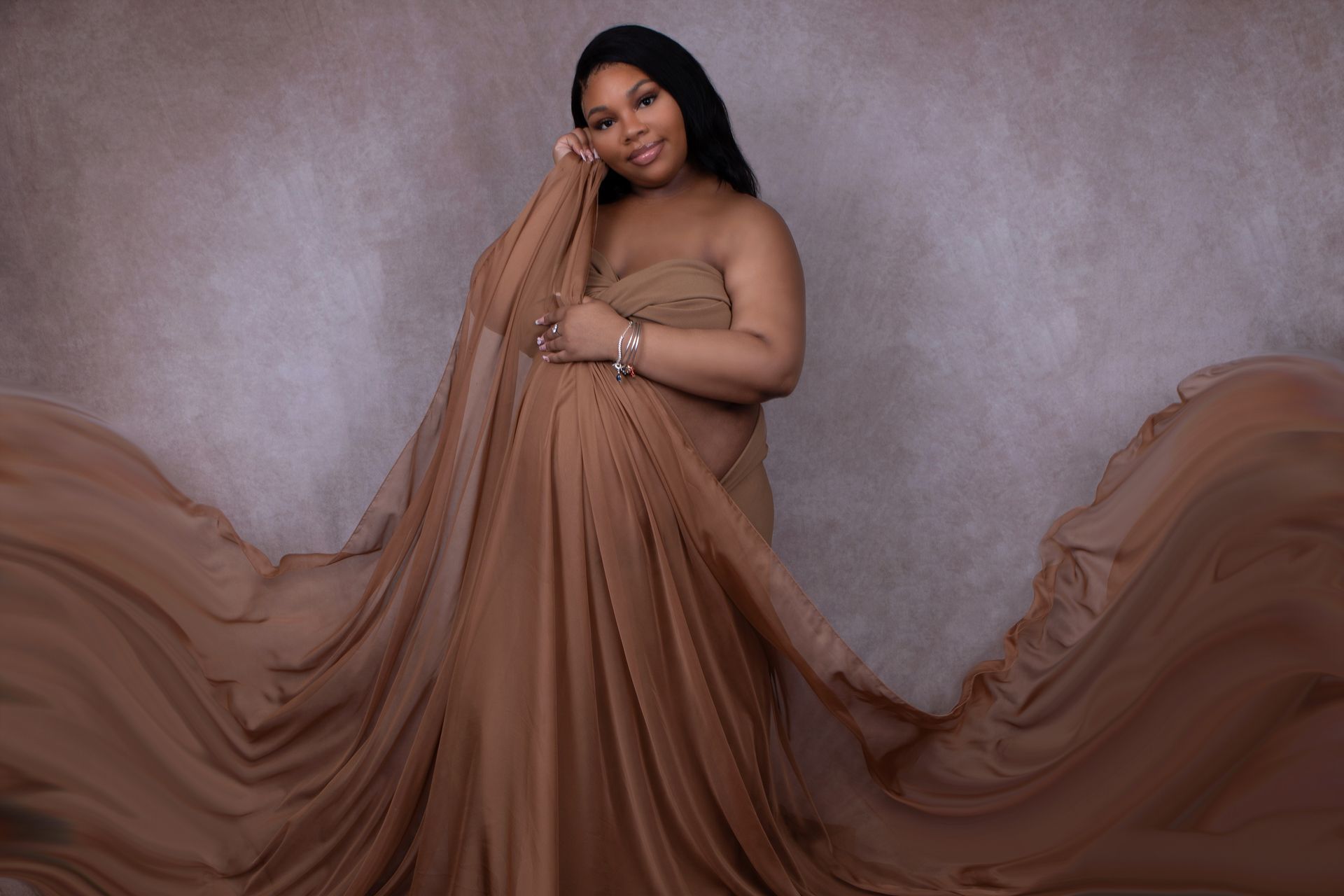 A pregnant woman is wearing a long brown dress