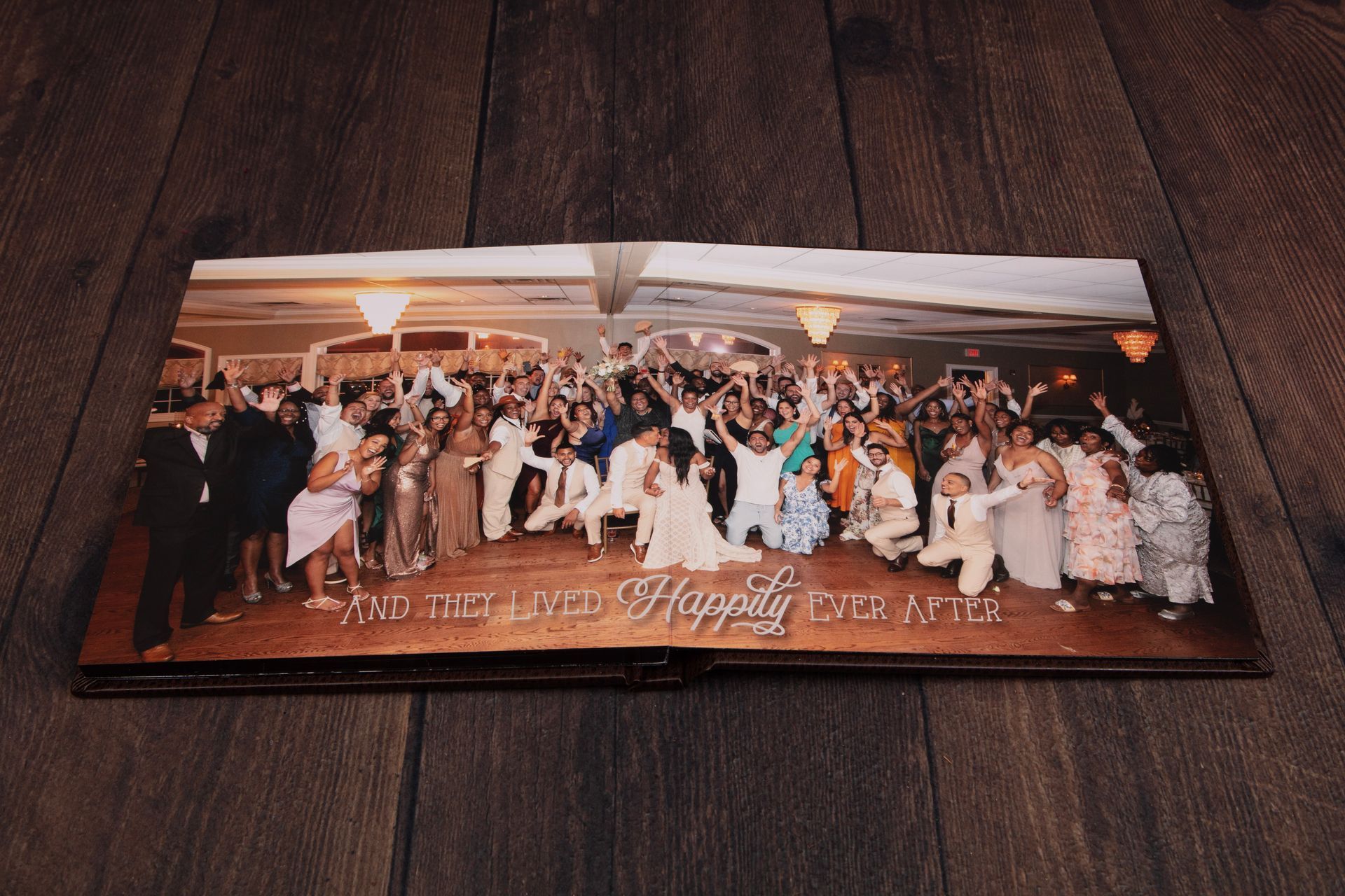 Wedding album opens with a large group photo of guests celebrating, with the bride and groom centered