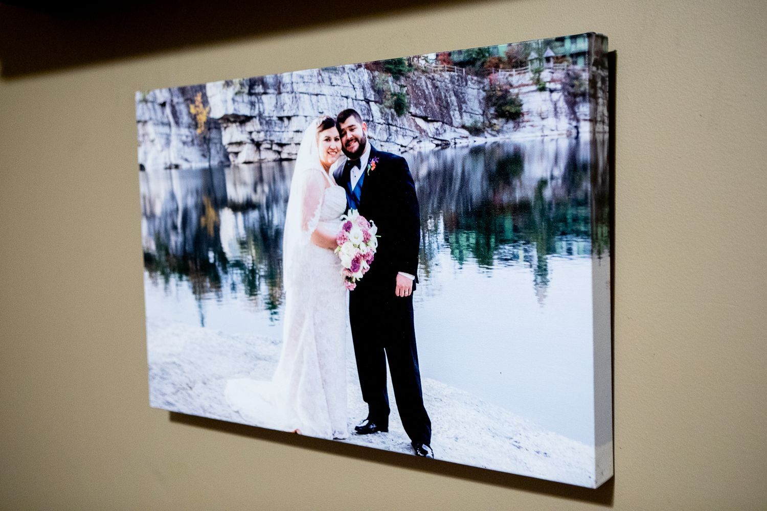 Bride and groom posing for wedding photo, hugging, in front of a lake, smiling.