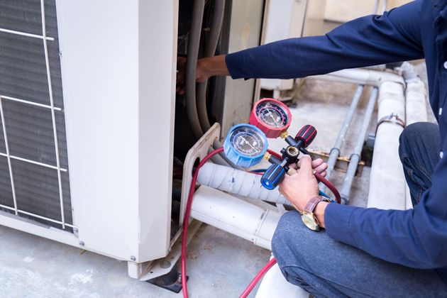 Person servicing an AC unit using gauges and hoses outdoors.