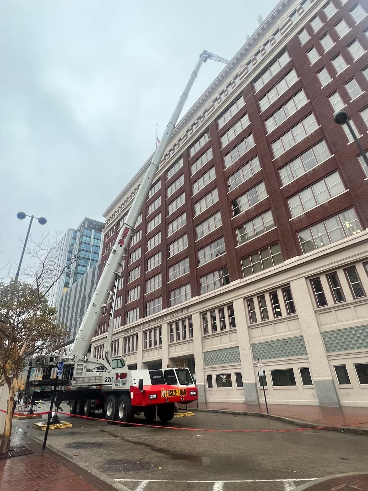 A crane reaching the top of a tall brick building on a cloudy day.