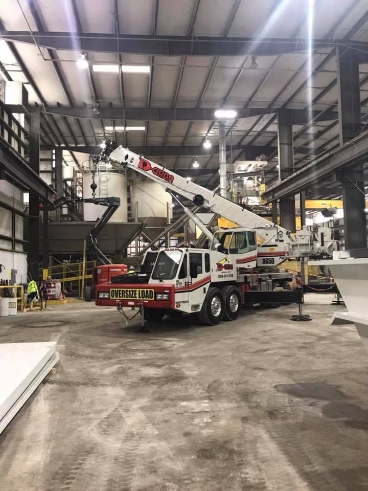 Crane inside a warehouse. White and red crane has arm extended. A worker is in the background.