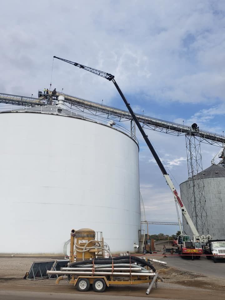 Crane extending over silos at a grain facility. A trailer with pipes sits in the foreground.