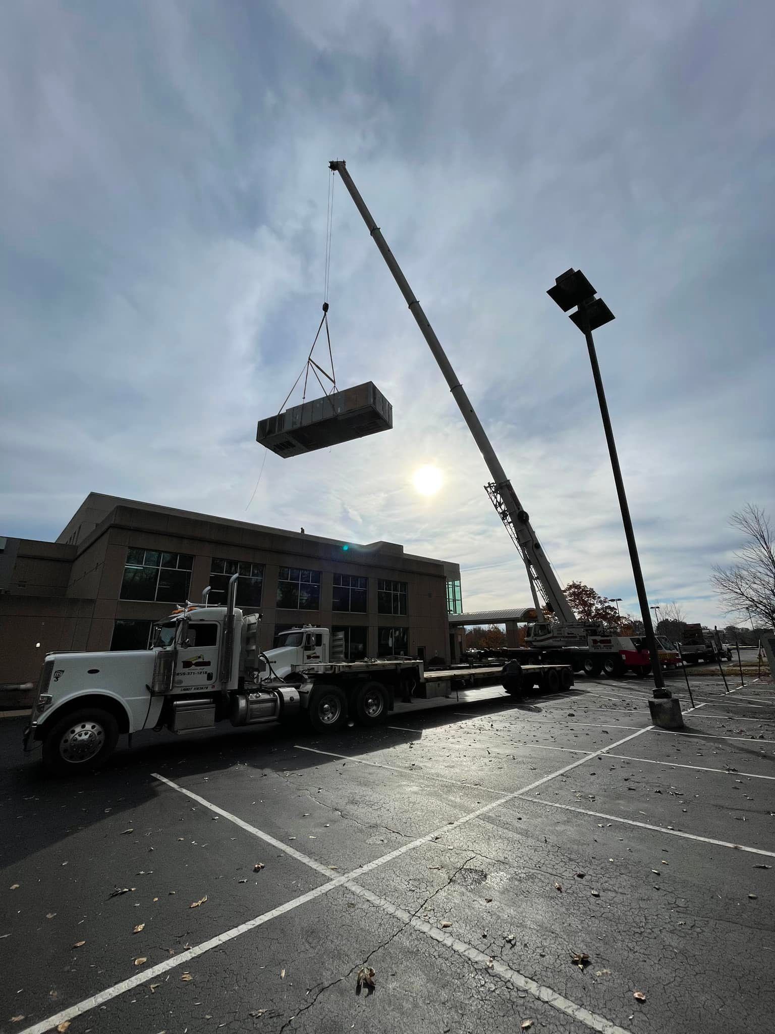 A crane lifting a large, rectangular object above a building. A truck is parked below.