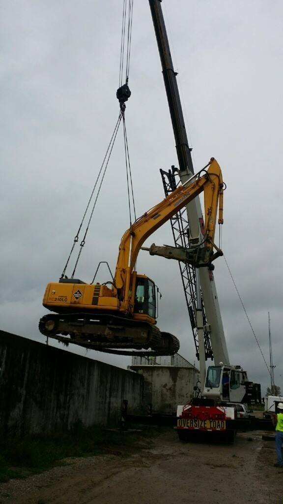 A yellow excavator being lifted by a crane at a construction site on a cloudy day.