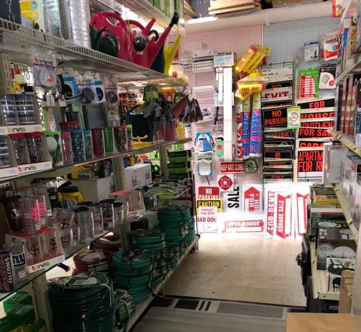 A cluttered hardware store aisle stocked with tools, hoses, and signs.