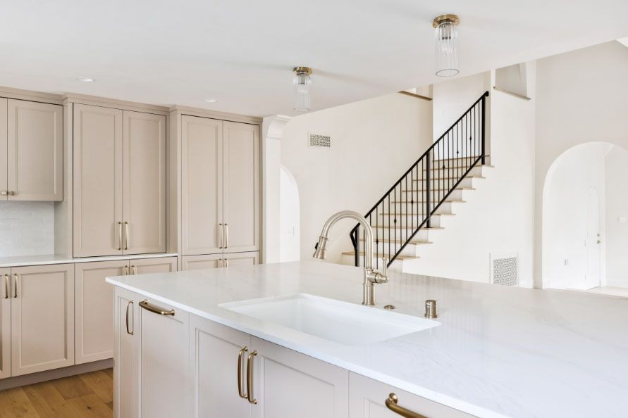 Bright modern kitchen with white cabinets, large island, and staircase in the background