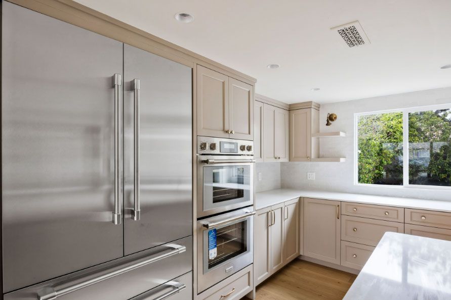 Modern white kitchen with stainless steel appliances, beige cabinets, and a bright window over the counter.