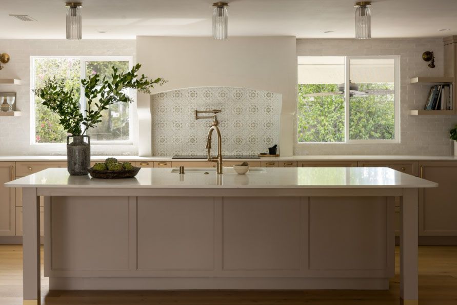 Bright modern kitchen with a large island, sink, pendant lights, and a vase of greenery by the window