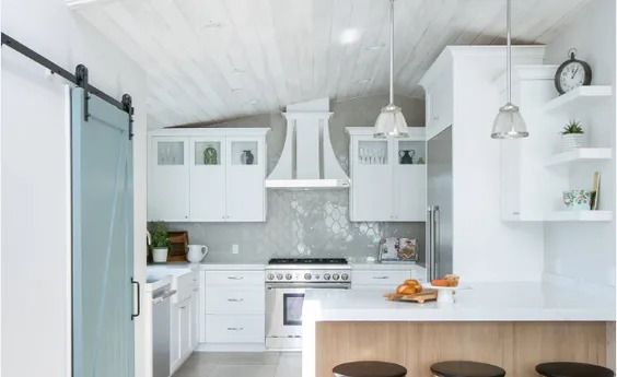 A bright kitchen featuring white cabinets, a light wood kitchen island with stools, and a blue sliding barn door.