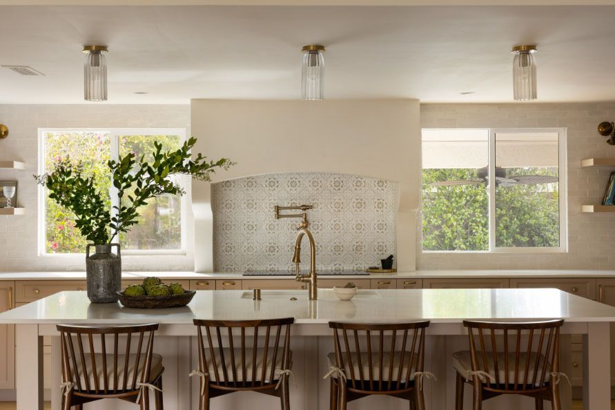 Bright kitchen with a large island, wooden stools, windows, and a vase of greenery.