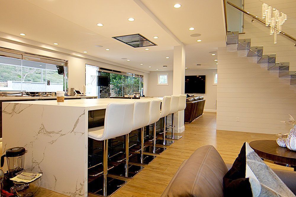 Modern, open-concept kitchen with a marble waterfall island, white bar stools, wood floors, and a staircase.
