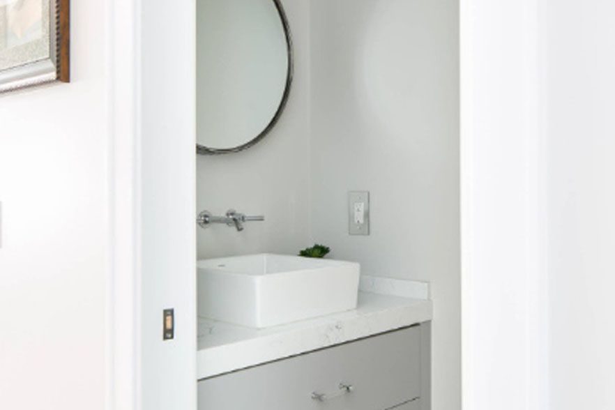 Small white bathroom vanity with sink, round mirror, and open door view