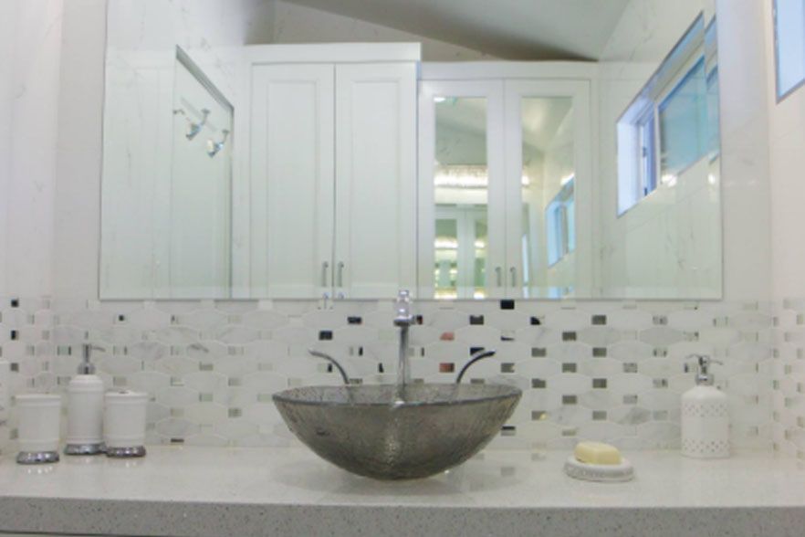Bright bathroom vanity with white cabinets, mosaic tile backsplash, and a vessel sink on a marble countertop.