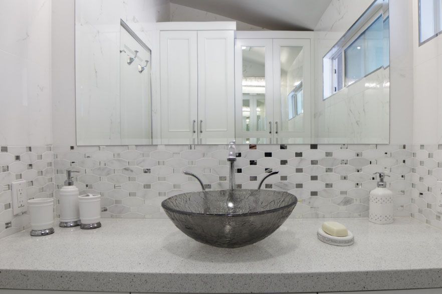 Bathroom vanity with double sinks, mirrored cabinets, and a large dark vessel basin on a white countertop.