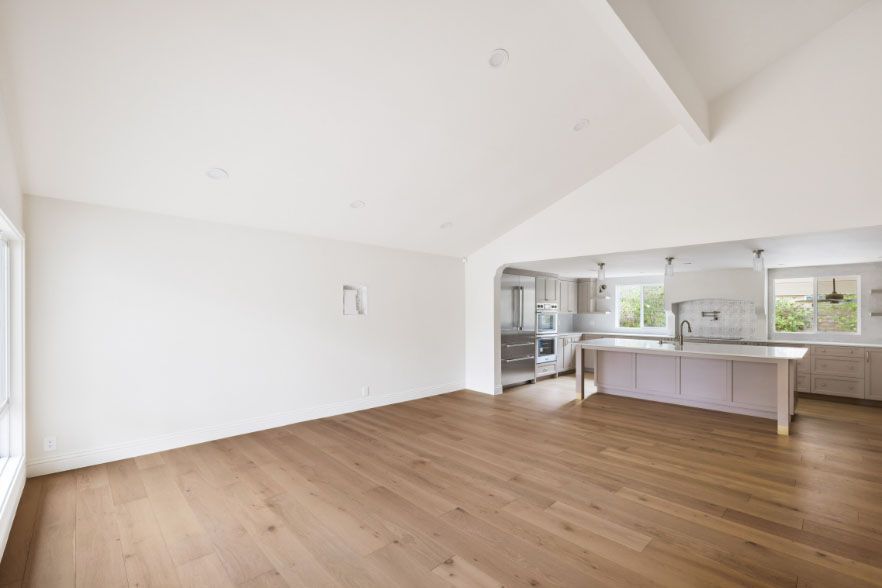 Bright open-plan kitchen and living area with white walls, wood floors, and a large island.