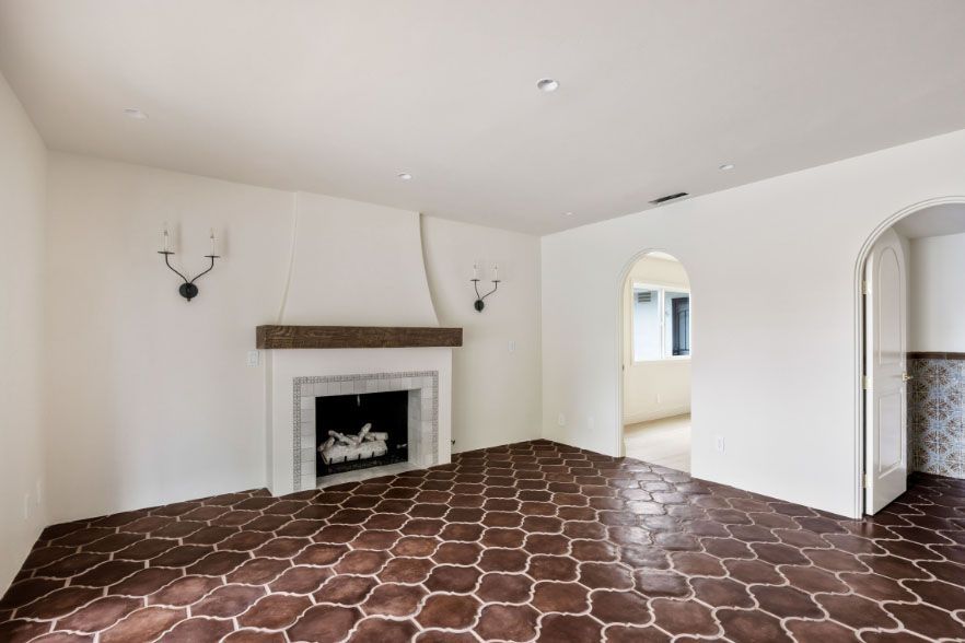 Empty living room with white walls, fireplace, arched doorways, and dark patterned tile floor
