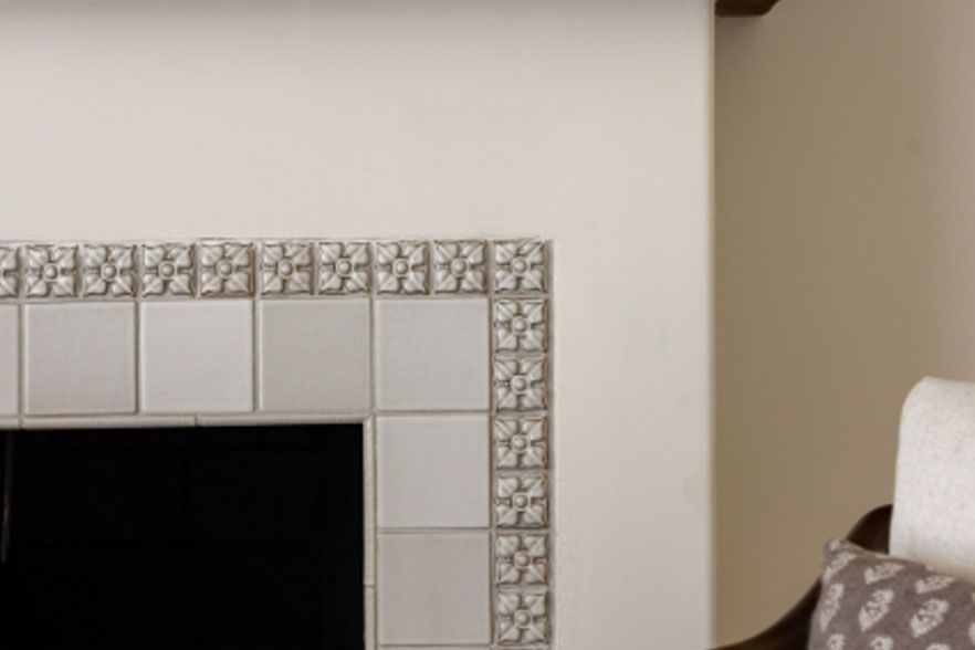Decorative tiled fireplace corner on a beige wall with a patterned chair at right